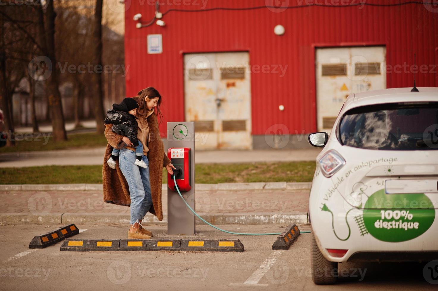 Young mother with child charging electro car at the electric gas station. photo