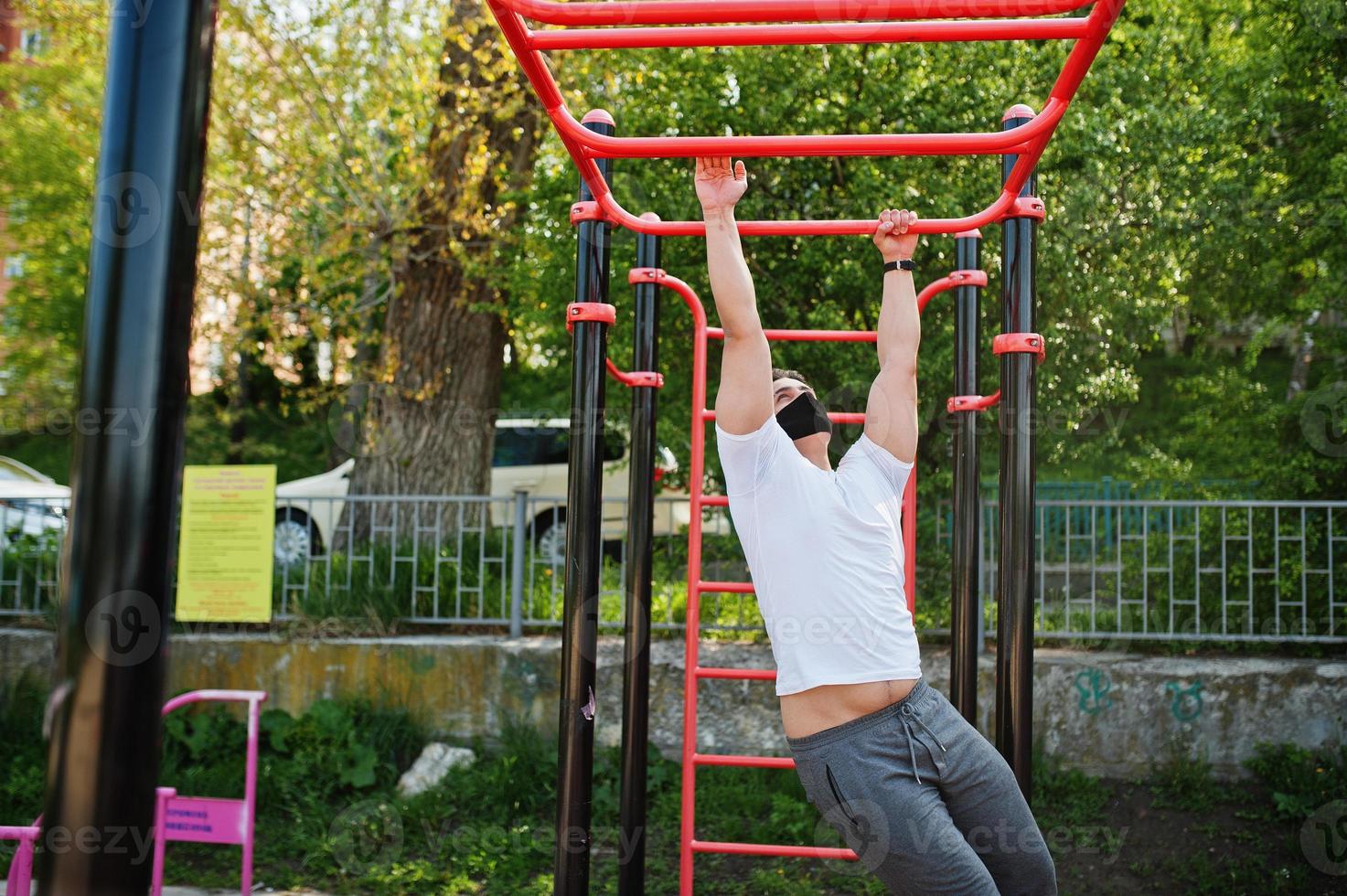 Portrait sports arabian man in black medical face mask doing workout exercises in outdoor gym place during coronavirus quarantine. photo