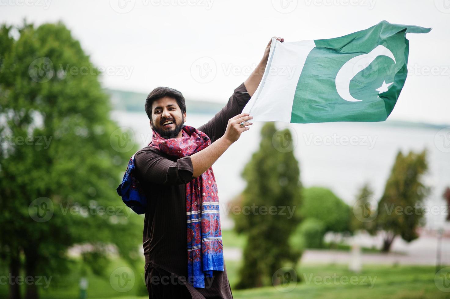 el hombre paquistaní usa ropa tradicional y sostiene la bandera de pakistán. foto