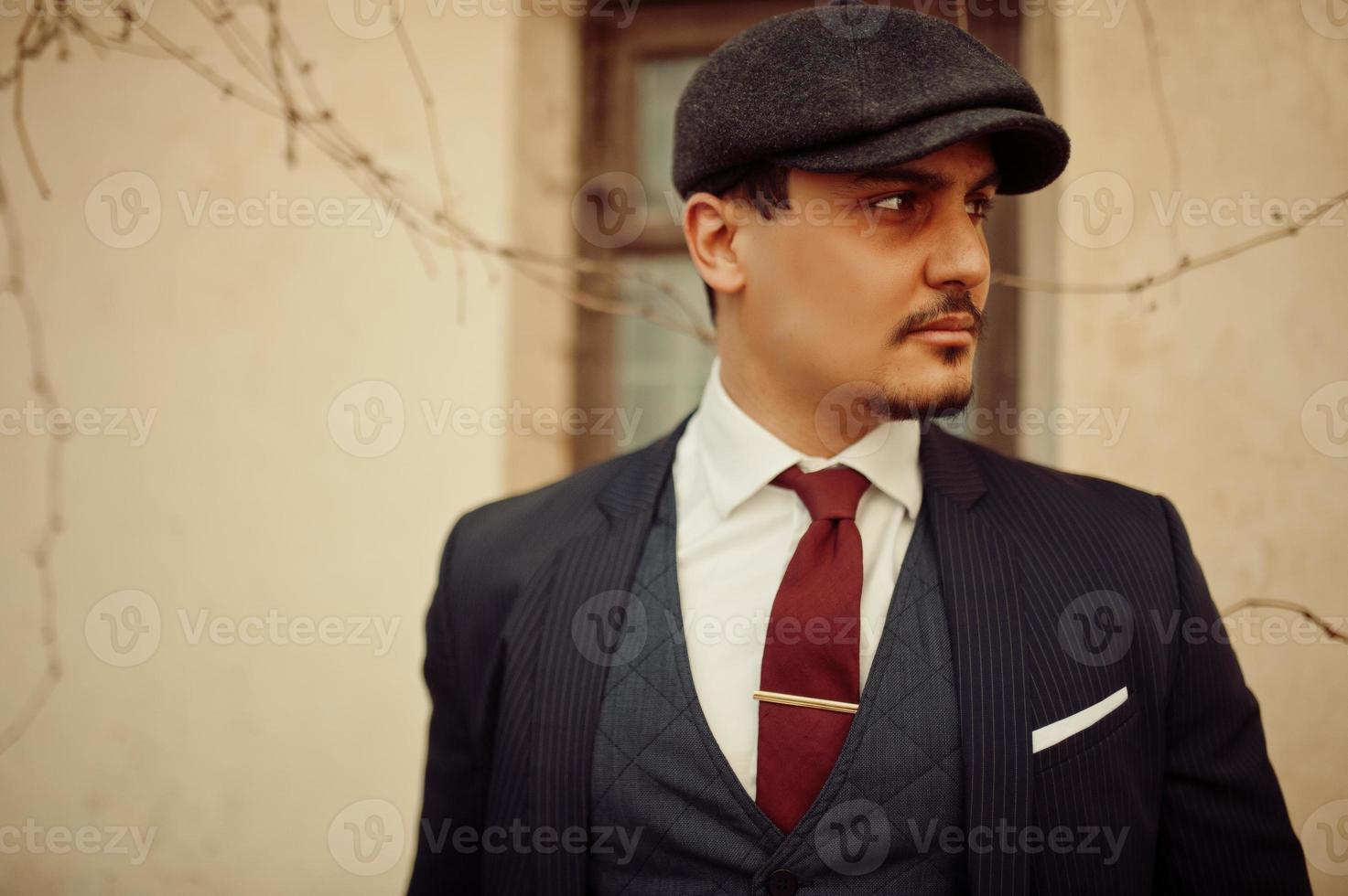 Portrait of retro 1920s english arabian business man wearing dark suit, tie and flat cap. photo