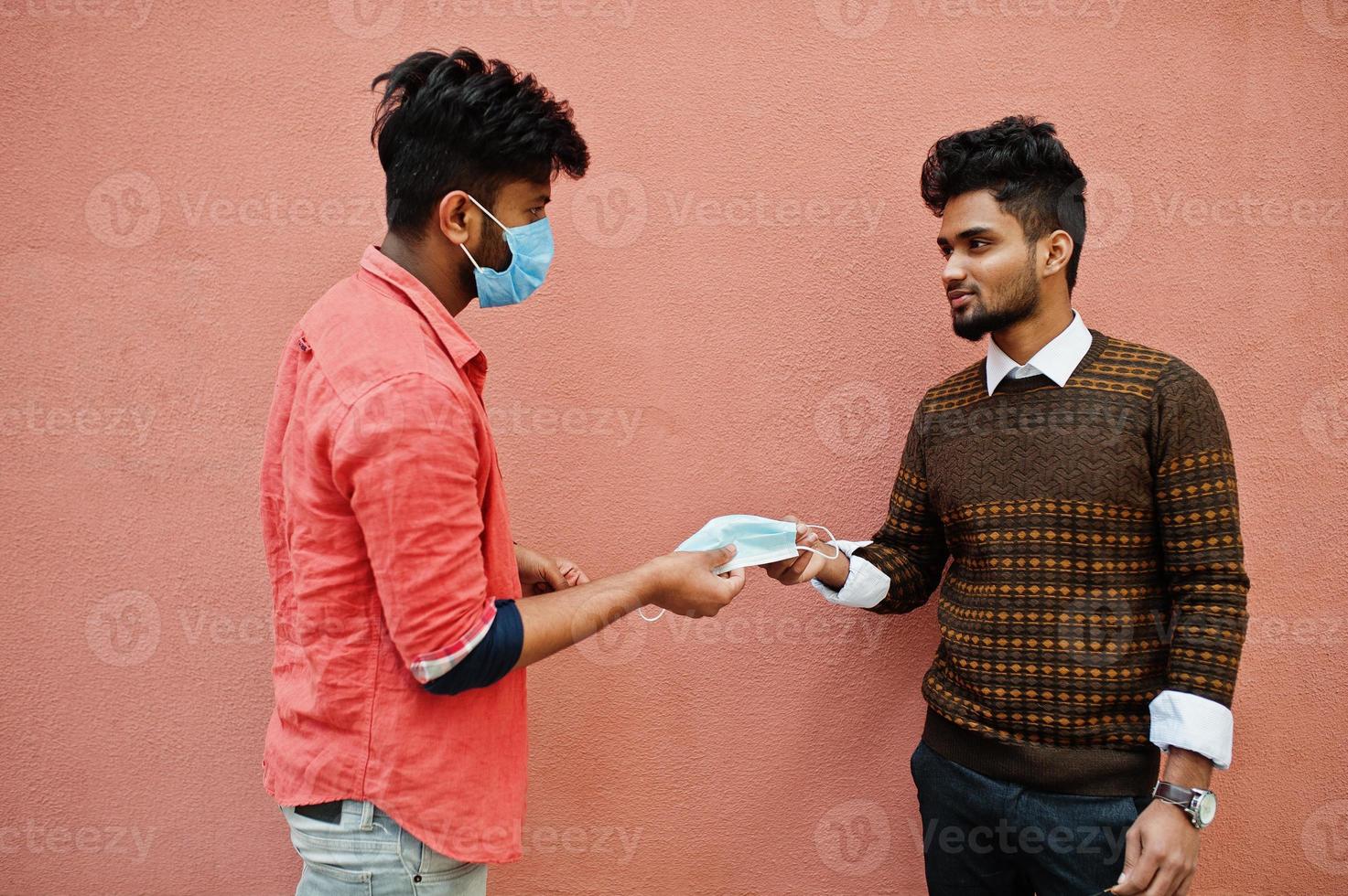 Coronavirus covid-19 concept. Two south asian indian man wearing mask for protect from corona virus isolated on pink background. Social distance. photo