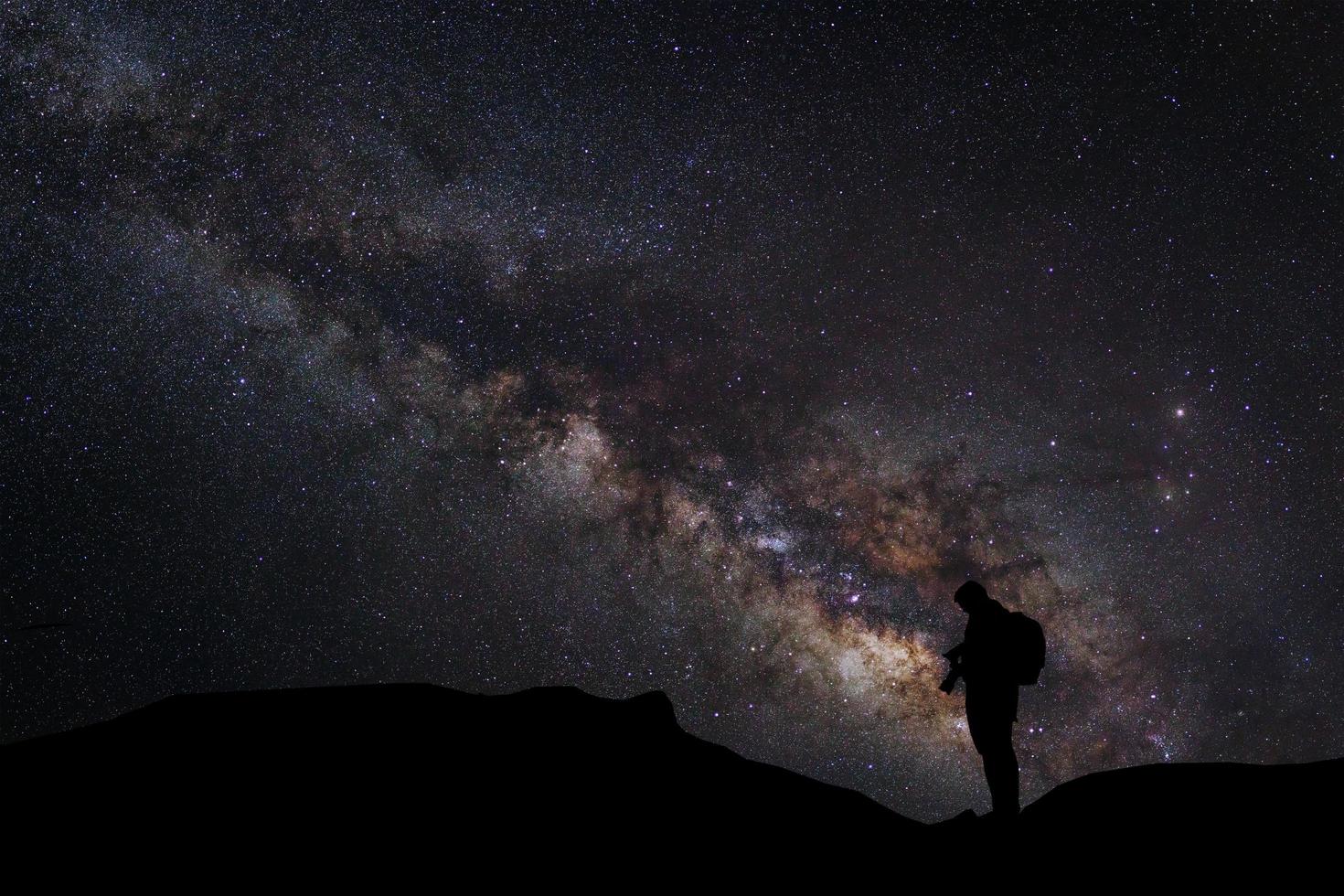 Landscape with milky way, Night sky with stars and silhouette of a standing photographer man on the mountain, Long exposure photograph, with grain photo