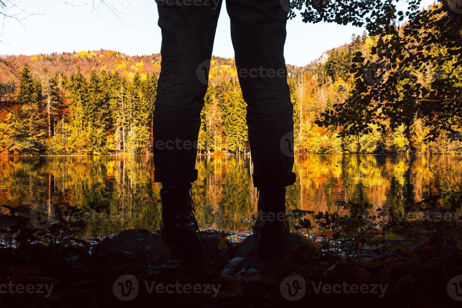 Close up low angle view silhouette of female legs and boots by scenic lake with outdoors in fall nature. Apparel in nature and autumn fashion concept photo