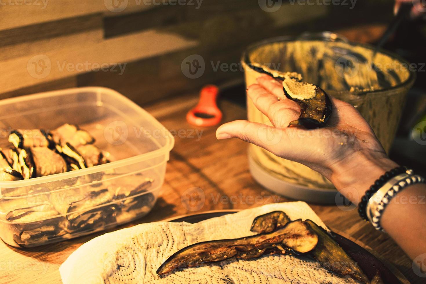las manos de las mujeres enrollan berenjenas con nueces untadas y las ponen en un recipiente de plástico en casa. preparación de platos tradicionales georgianos foto