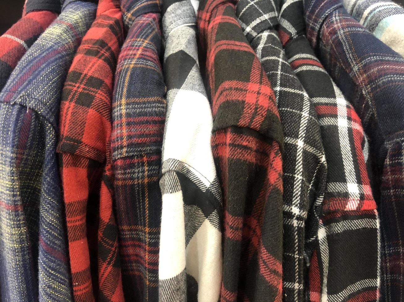 brightly colored plaid vintage flannel shirts nestled together on the hook of a clothing store distro photo