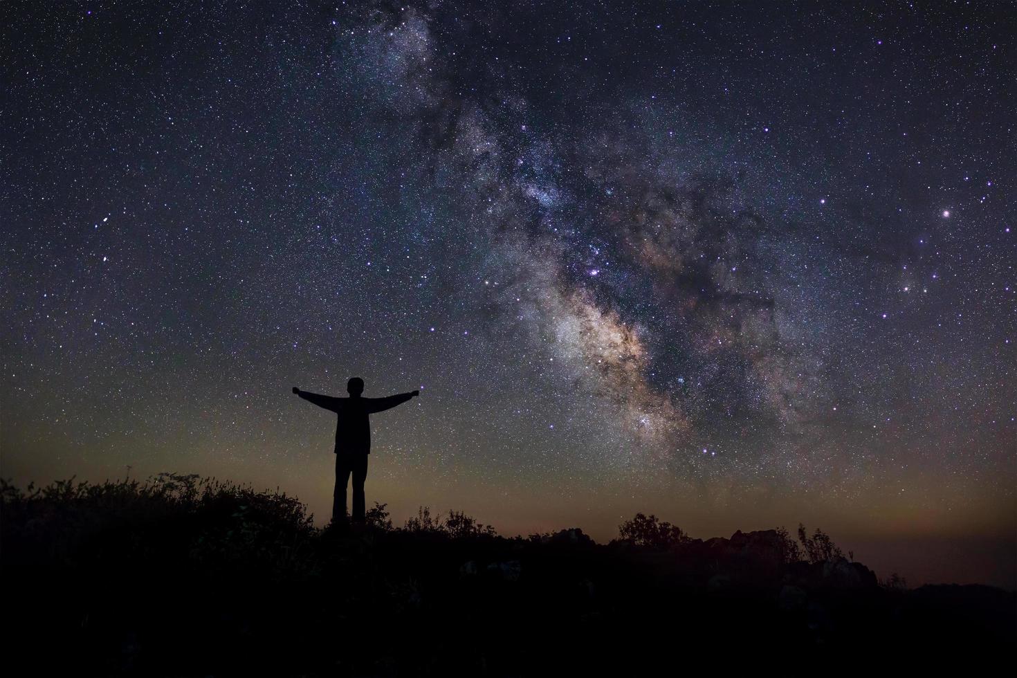 Landscape with milky way, Night sky with stars and silhouette of a standing happy man on the mountain, Long exposure photograph, with grain photo