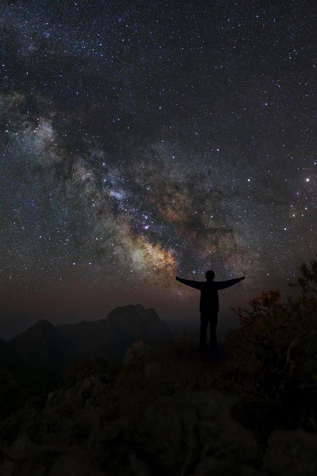 un hombre está de pie junto a la galaxia de la vía láctea apuntando a una estrella brillante, fotografía de larga exposición, con grano foto