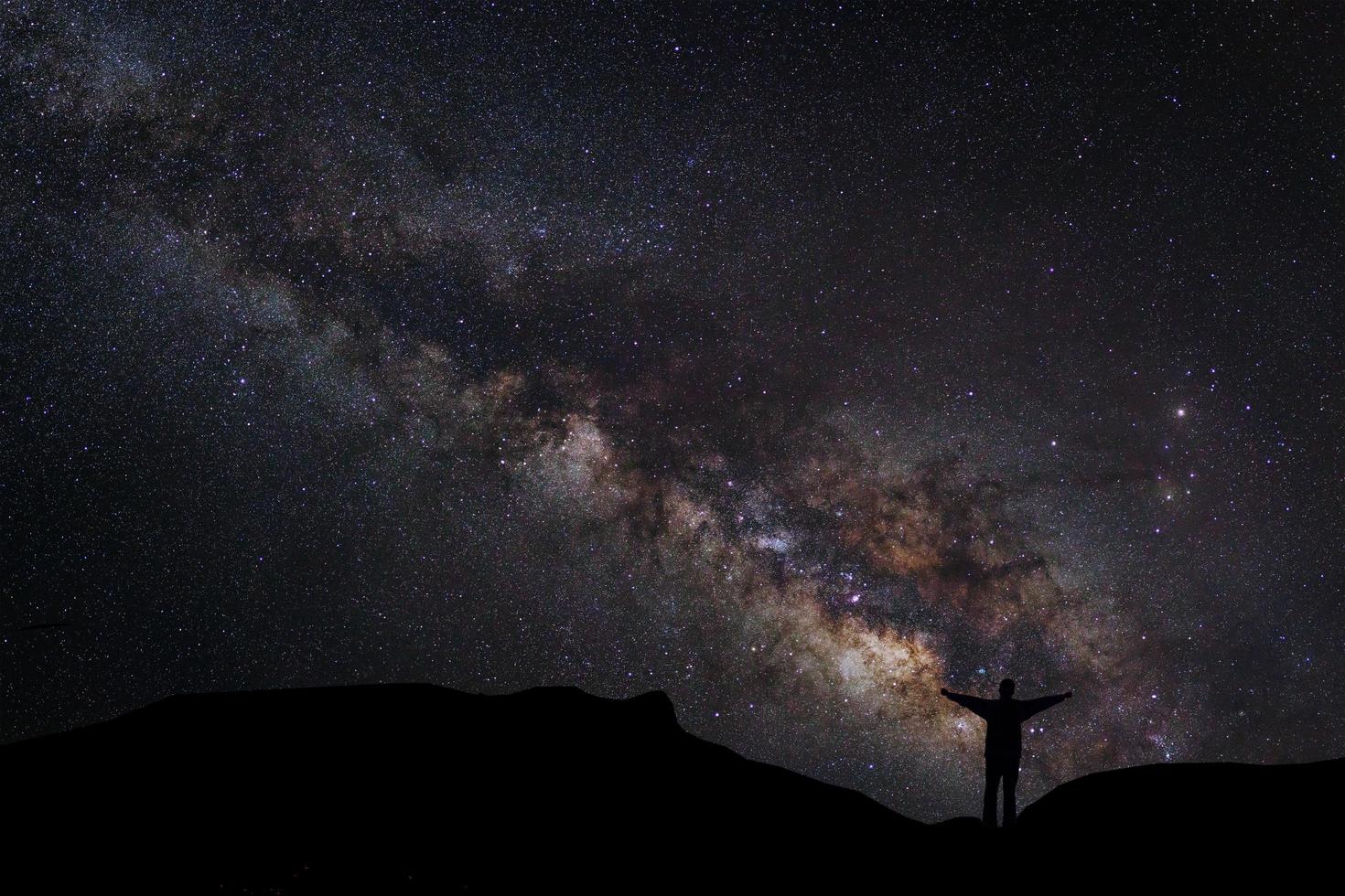 paisaje con vía láctea, cielo nocturno con estrellas y silueta de un hombre feliz de pie en la montaña, fotografía de larga exposición, con grano foto