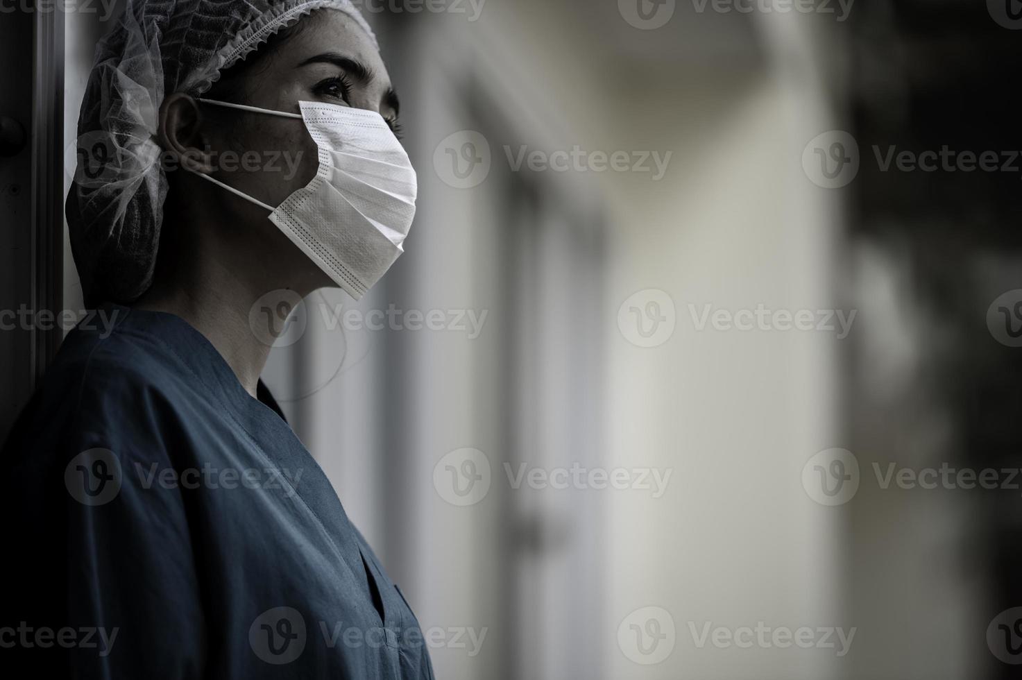 Tired depressed female asian scrub nurse wears face mask blue uniform sits on hospital floor,Young woman doctor stressed from hard work photo