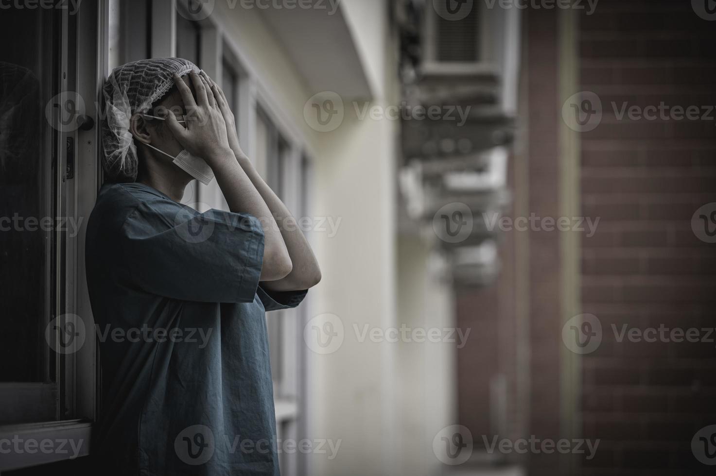 una enfermera asiática cansada y deprimida usa una máscara facial uniforme azul sentada en el piso del hospital, una joven doctora estresada por el trabajo duro foto