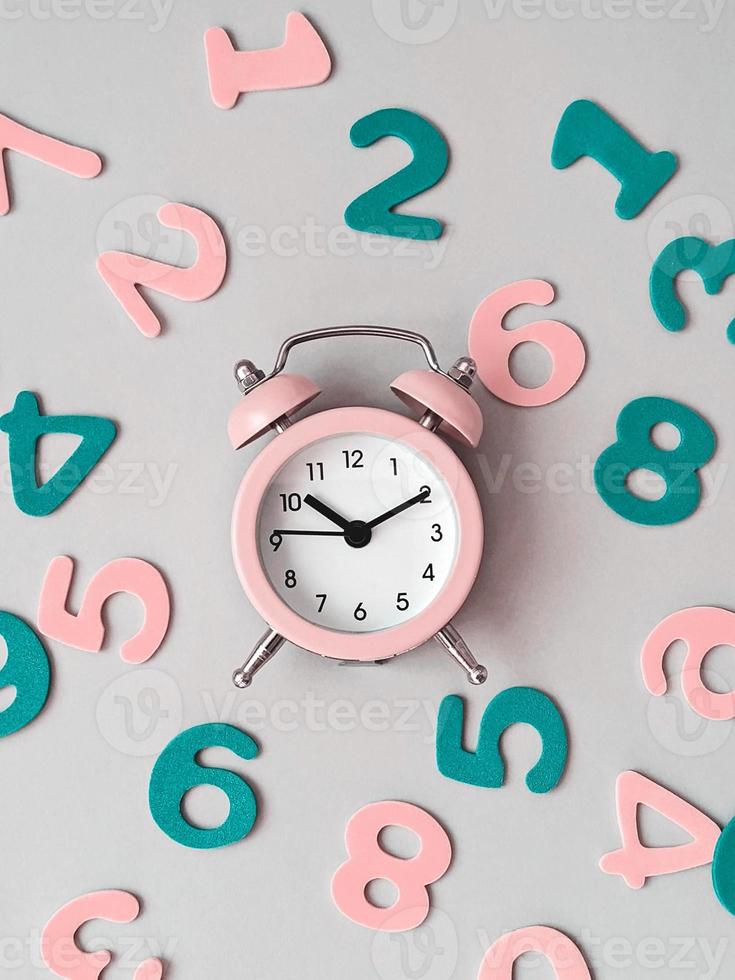 Pink alarm clock on pink background with colorful numbers flat lay. Back to school concept photo