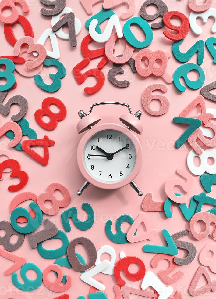 Pink alarm clock on pink background with colorful numbers flat lay. Back to school concept. photo
