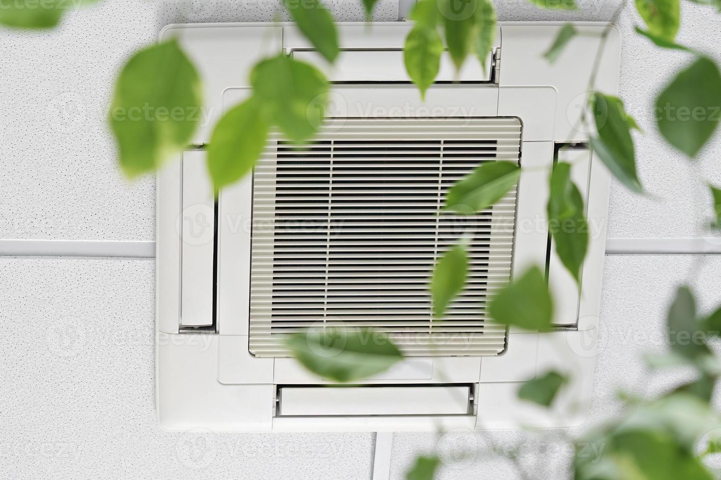 Closeup cassette Air Conditioner on ceiling in modern light office or apartment with green ficus plant leaves. Indoor air quality photo