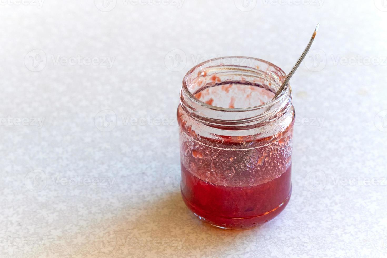 Glass jar of jam that has almost been eaten. photo