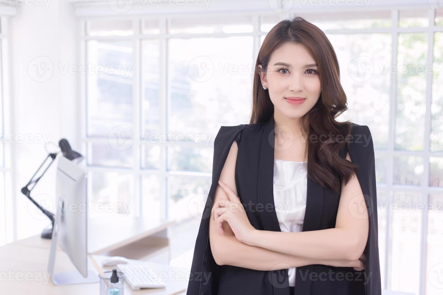 Asian confident working woman who has a long hair with a black suit is standing and arm crossing in work from home concept. photo