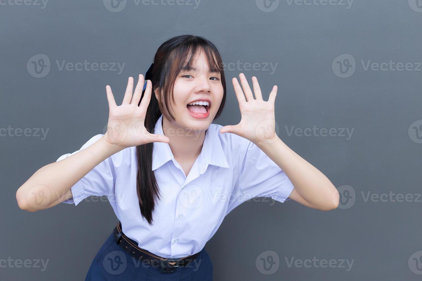 Beautiful Asian high school student girl in the school uniform with smiles confidently while she looks at the camera happily with grey in the background. photo