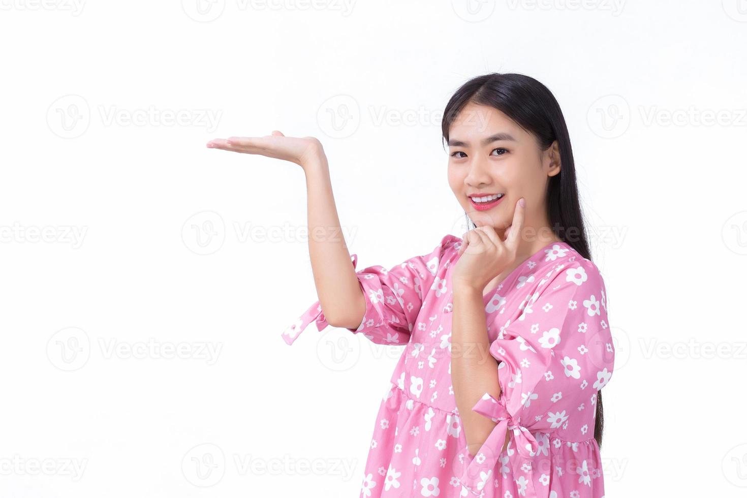 Asian beautiful woman with black long hair in pink shirt shows present something on white background. photo