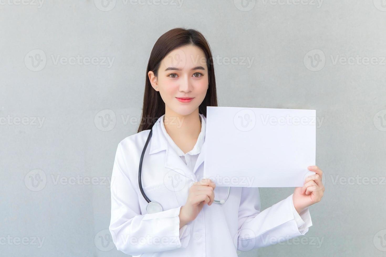 Asian woman doctor who wears medical coat holds and shows white paper to present something in healthcare concept. photo