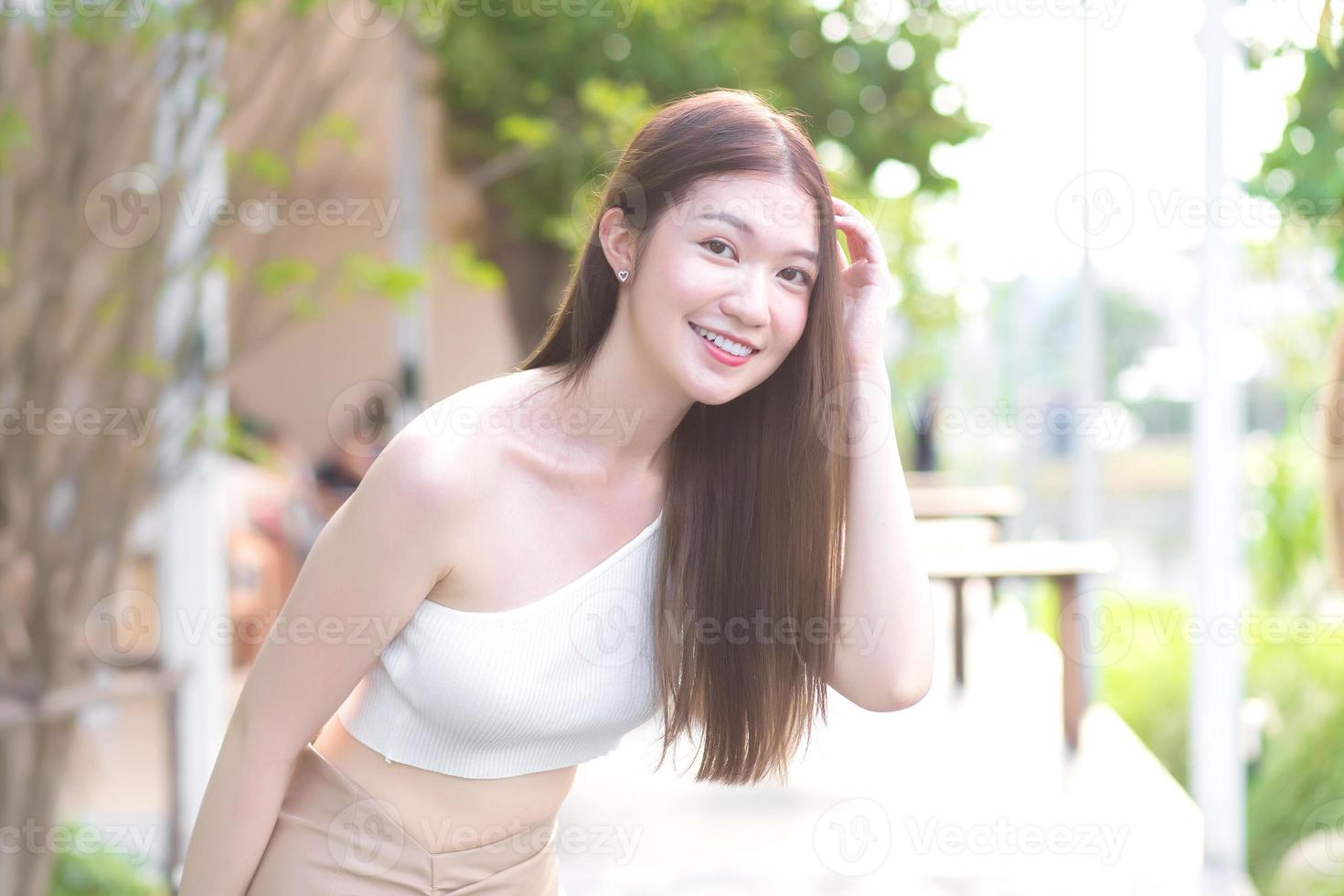 joven mujer asiática hermosa con buena piel en camisa crema de pie sonriendo felizmente en un fondo borroso. foto