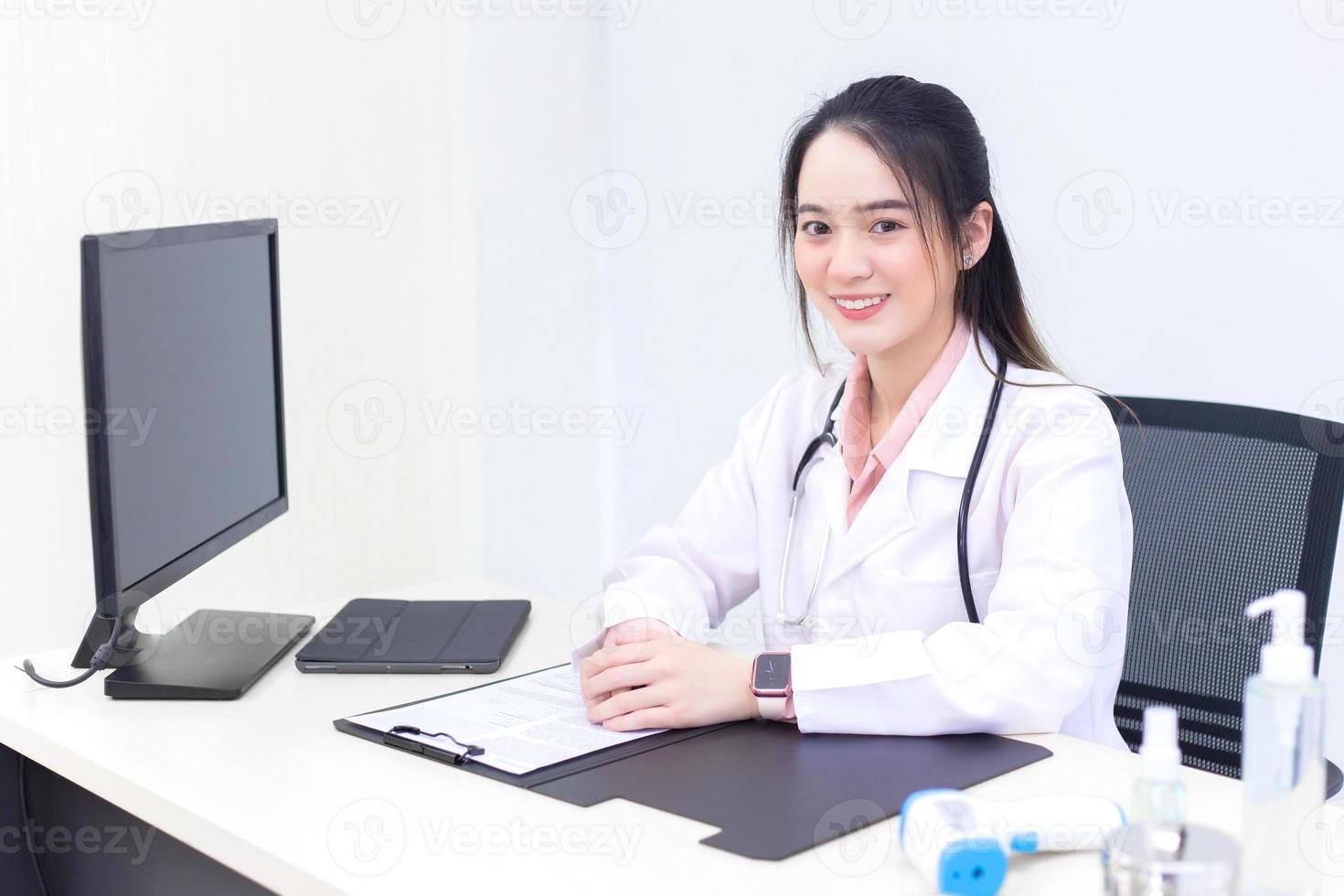 Asian young woman doctor in a white lab coat is sitting on office room at hospital photo