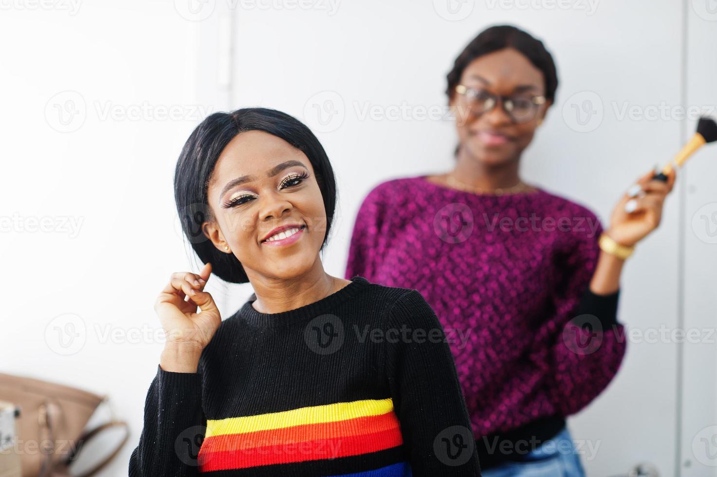 African American woman applying make-up by make-up artist at beauty saloon. photo