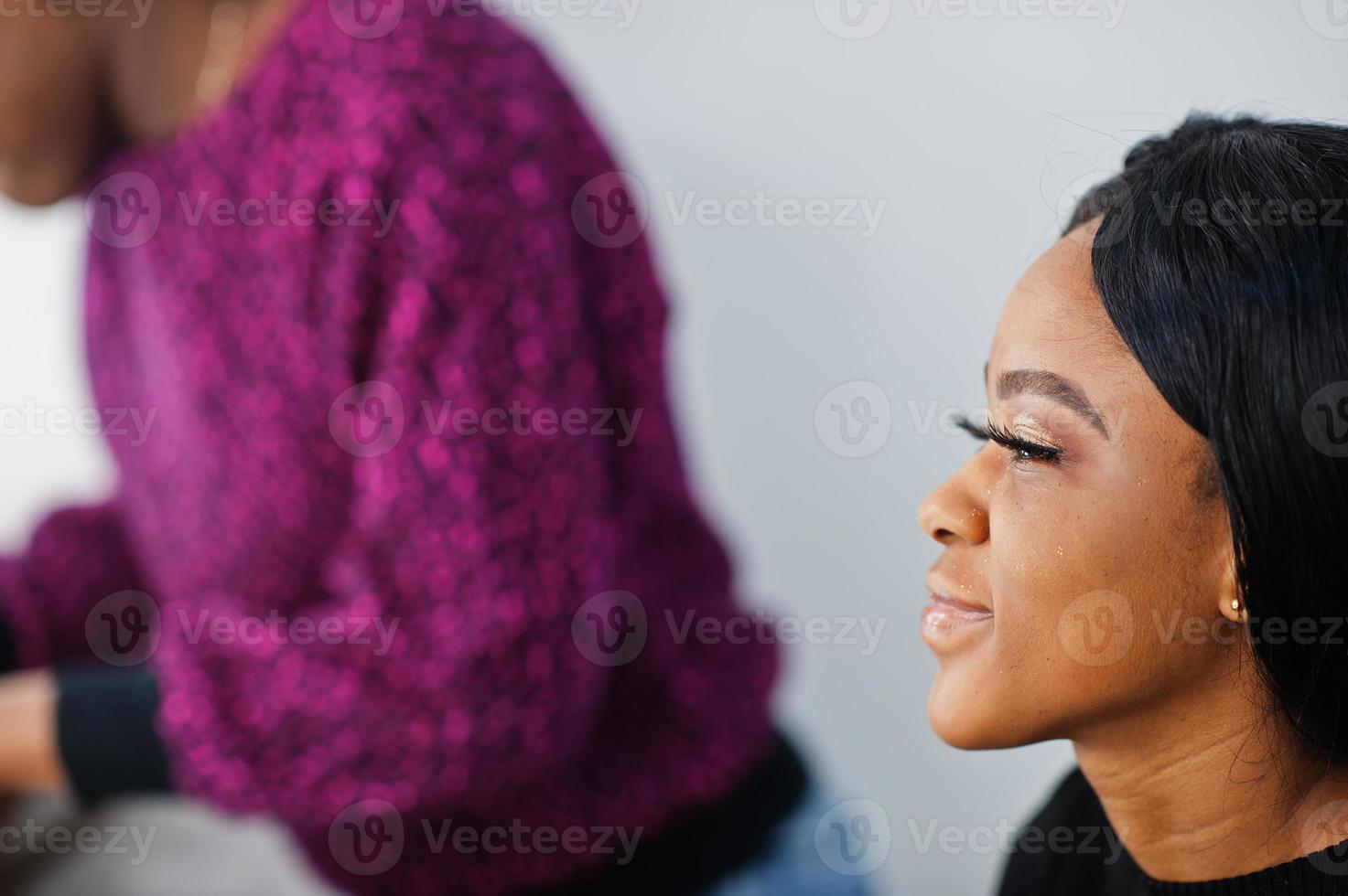 African American woman applying make-up by make-up artist at beauty saloon. photo