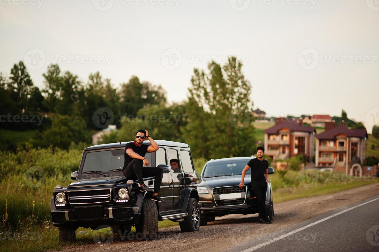 Two asian brothers man wear on all black posed near suv cars. photo