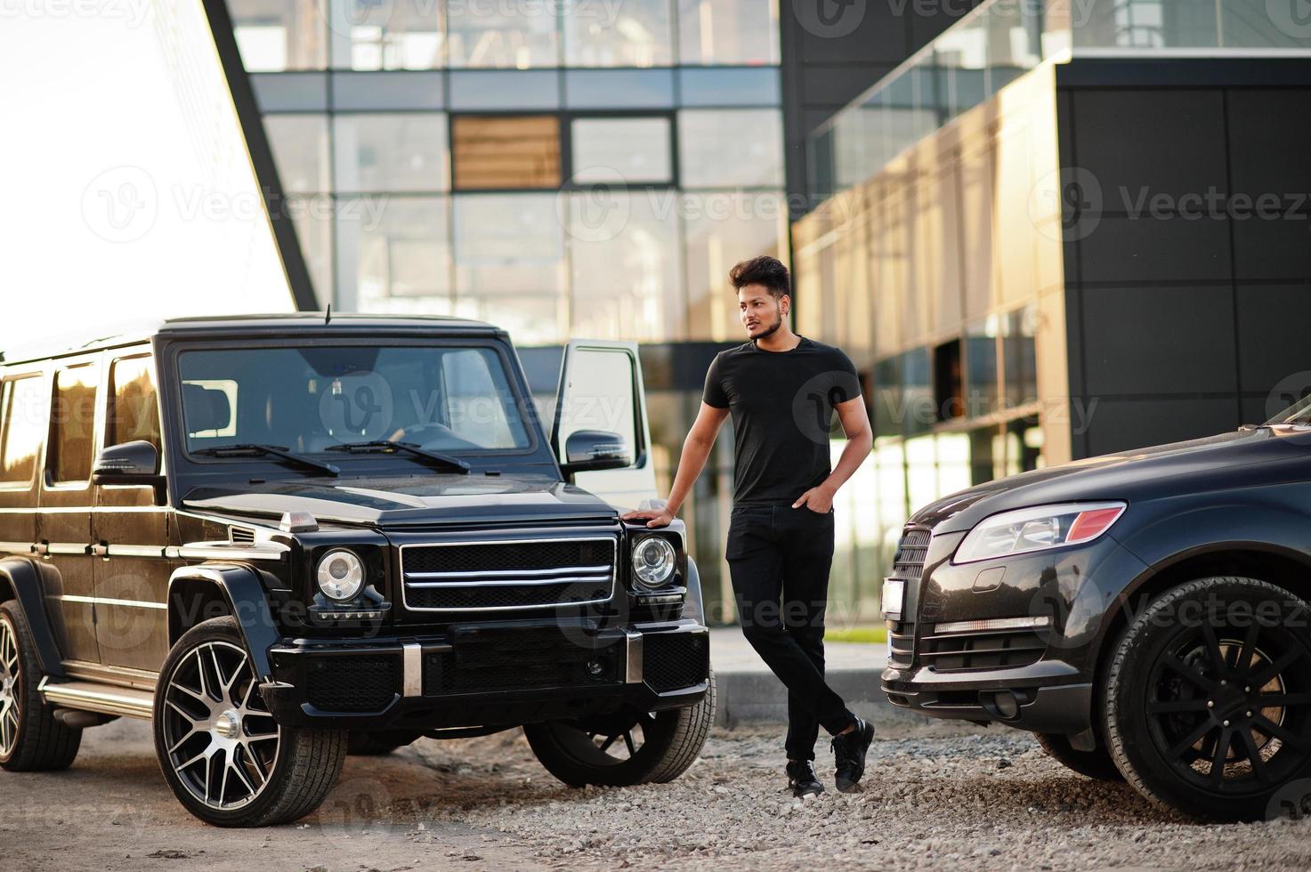 Asian man wear on all black posed near suv car. photo