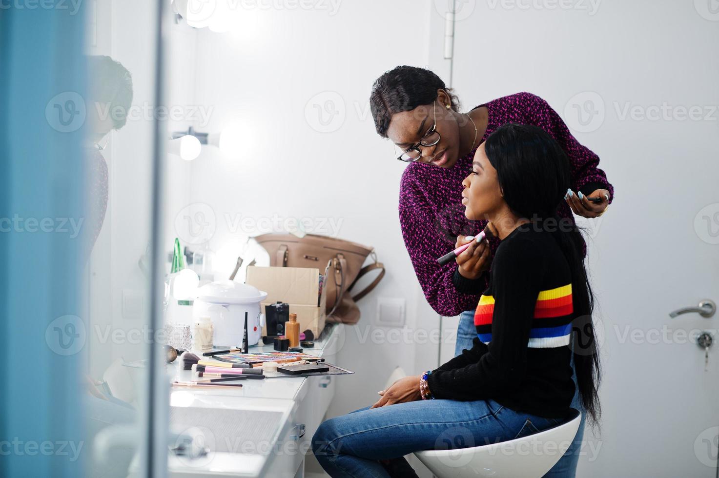 African American woman applying make-up by make-up artist at beauty saloon. photo