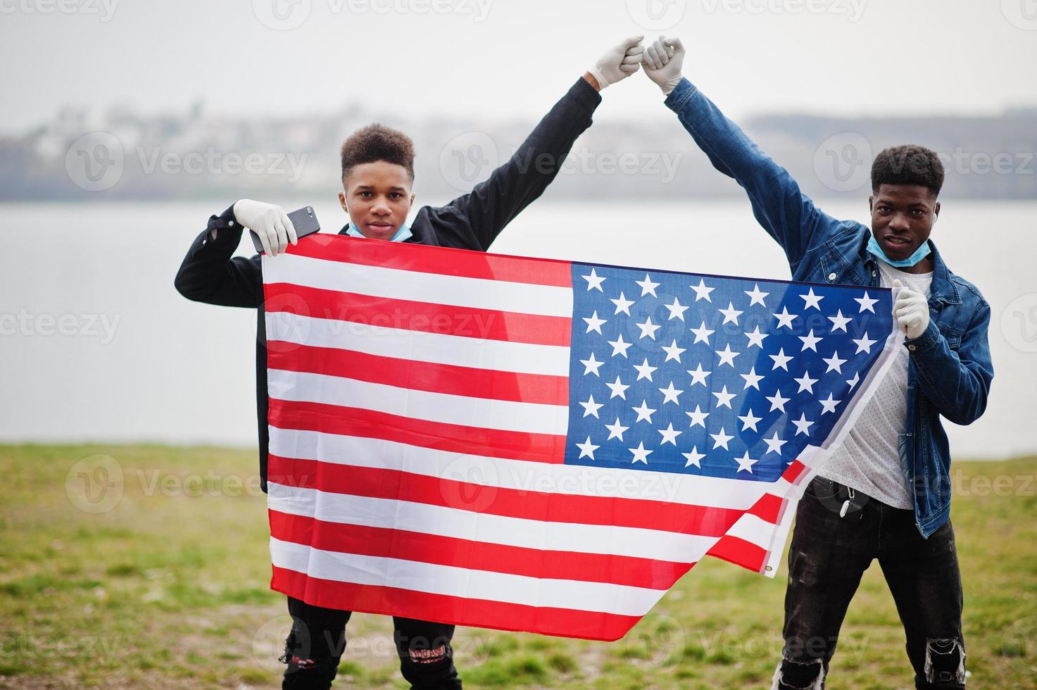 Two african teenagers friends with american flag at park wearing medical masks protect from infections and diseases coronavirus virus quarantine. photo