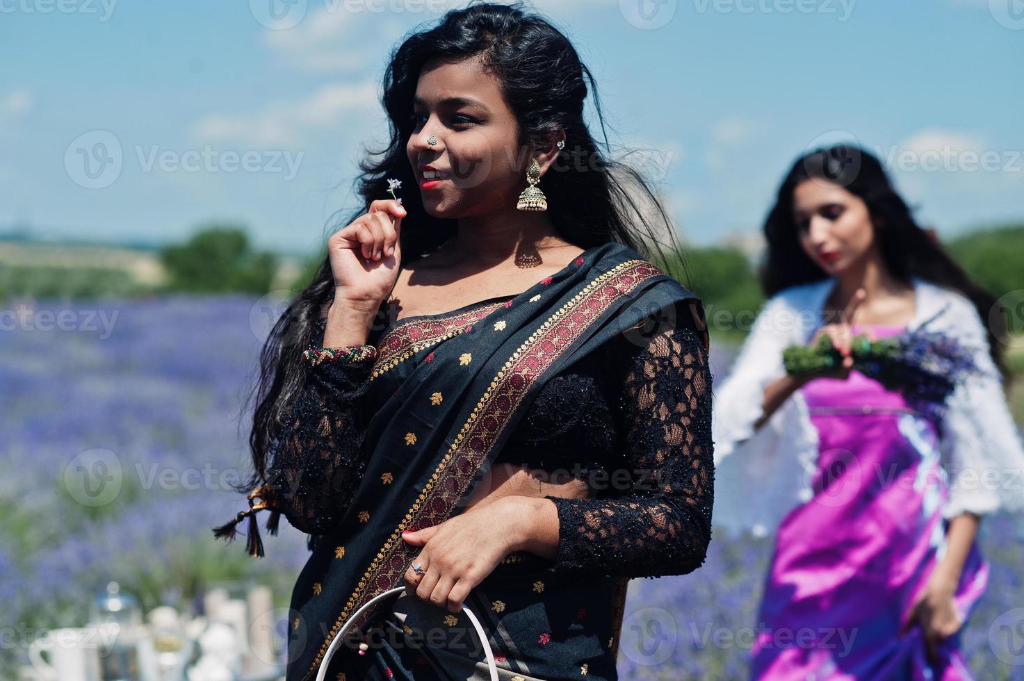 dos hermosas chicas indias visten un vestido tradicional saree india en un campo de lavanda púrpura. foto