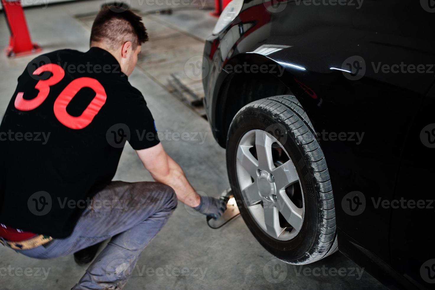 Car repair and maintenance theme. Mechanic in uniform working in auto service, checking tyres. photo