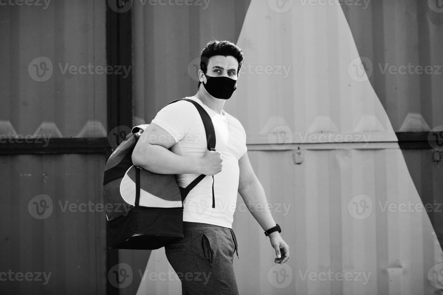 Portrait sports arabian man in black medical face mask with backpack posed against yellow triangle during coronavirus quarantine. photo