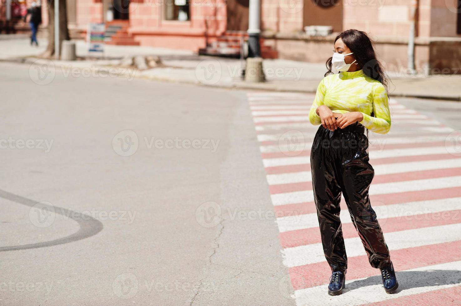 African American woman posing with facial mask to protect from infections from bacteria, viruses and epidemics, standing on pedestrian crosswalk. photo