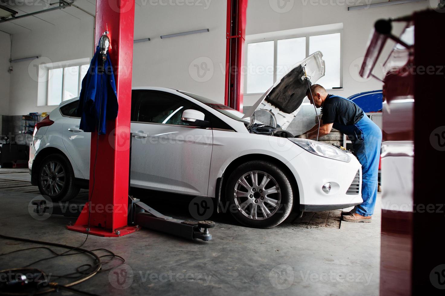 Car repair and maintenance theme. Mechanic in uniform working in auto service, checking engine. photo