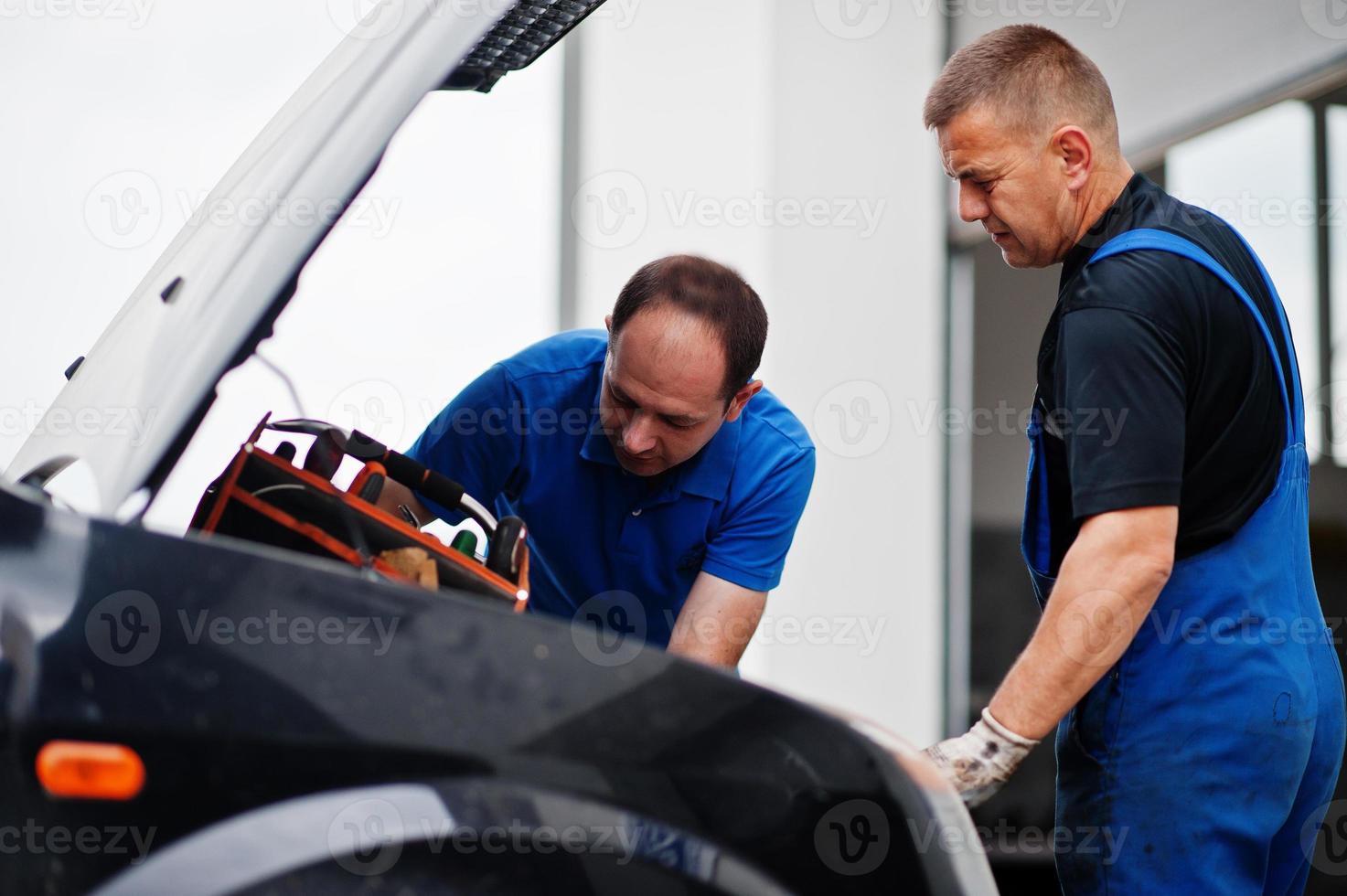 Car repair and maintenance theme. Two mechanics in uniform working in auto service, checking engine. photo