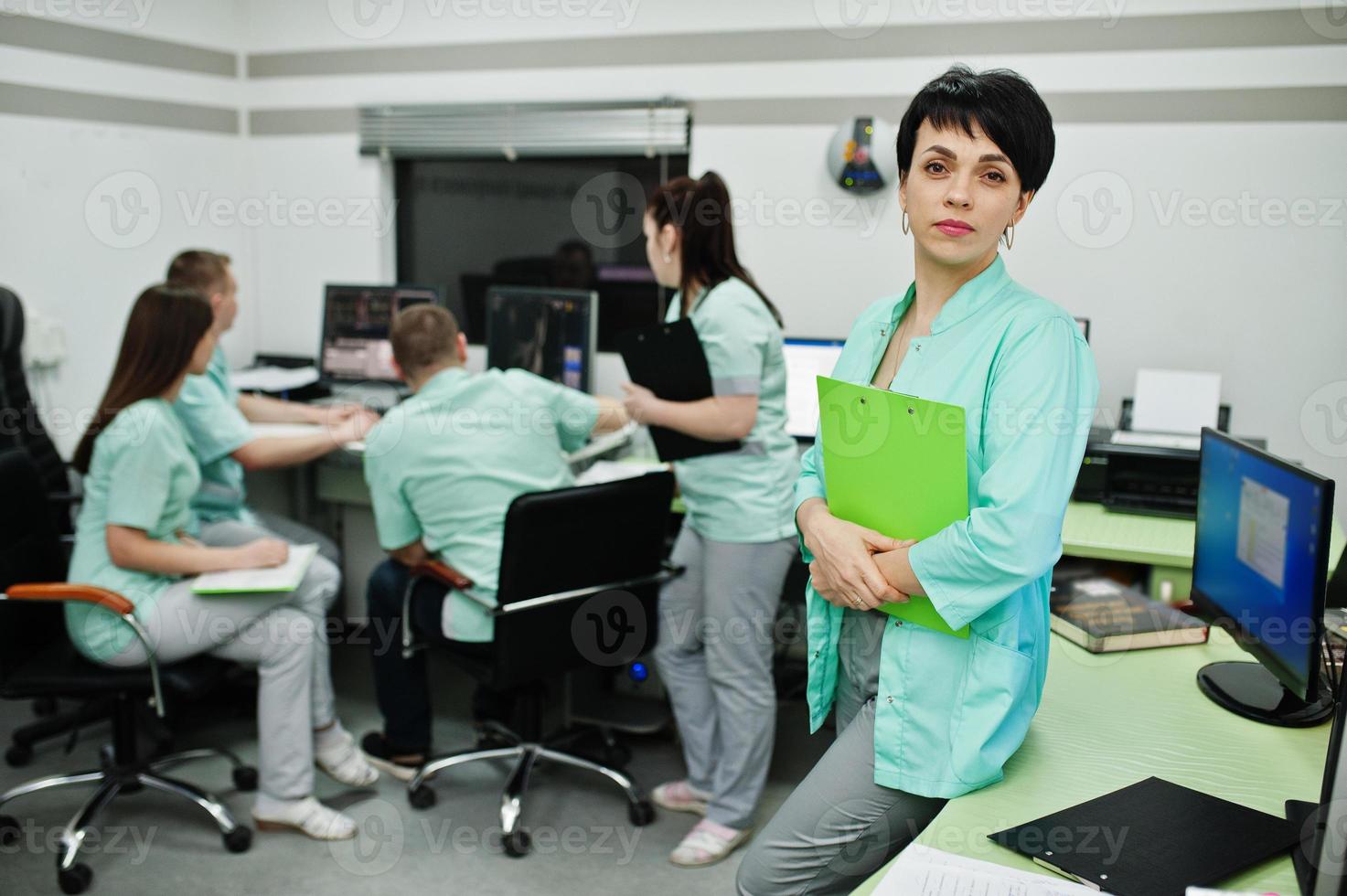 Medical theme .Portrait of female doctor with clipboard against group of doctors meeting in the mri office at diagnostic center in hospital. photo