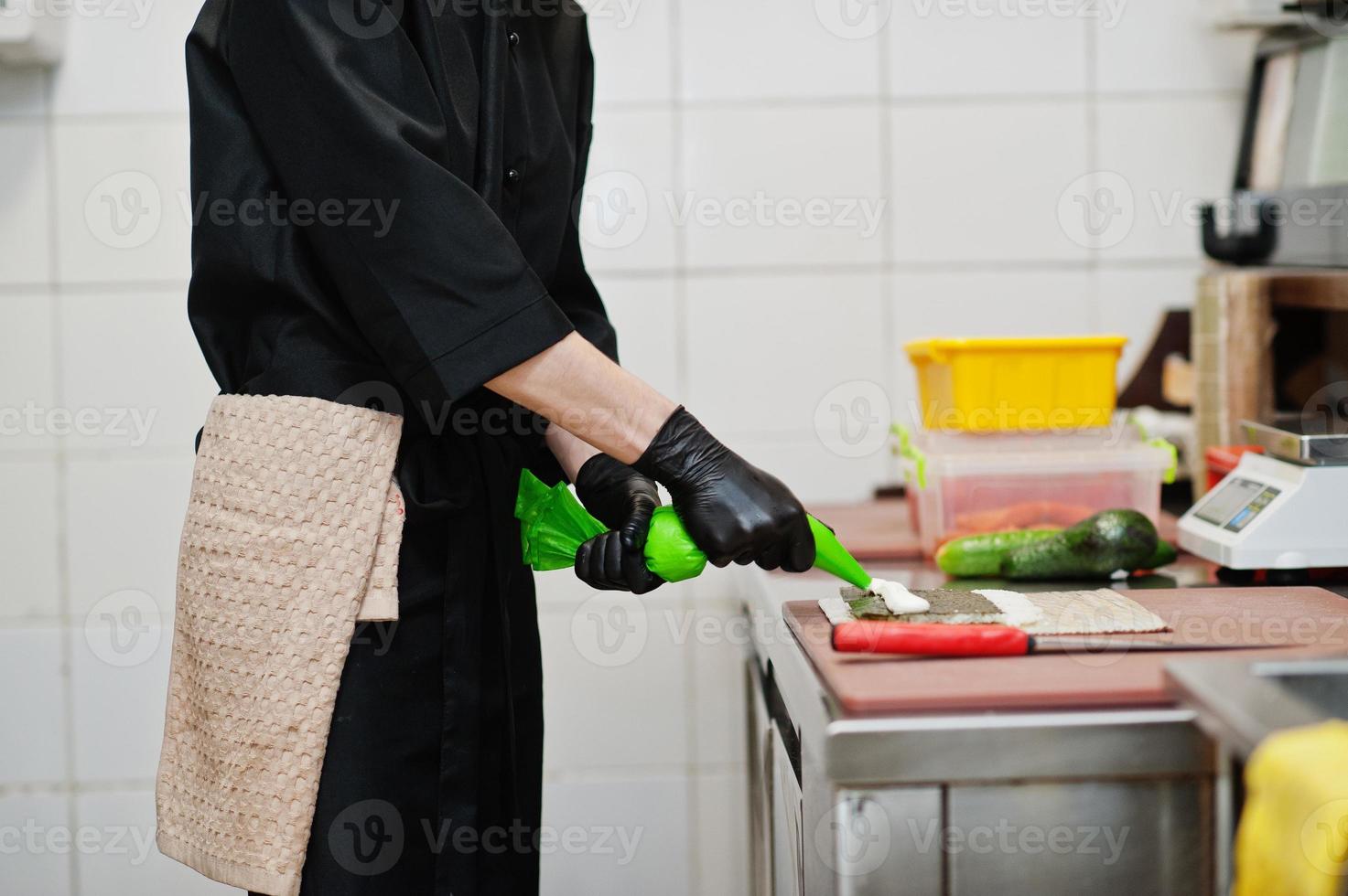 Cierra las manos de un chef profesional con guantes negros haciendo sushi y rollos en la cocina de un restaurante de comida tradicional japonesa. foto