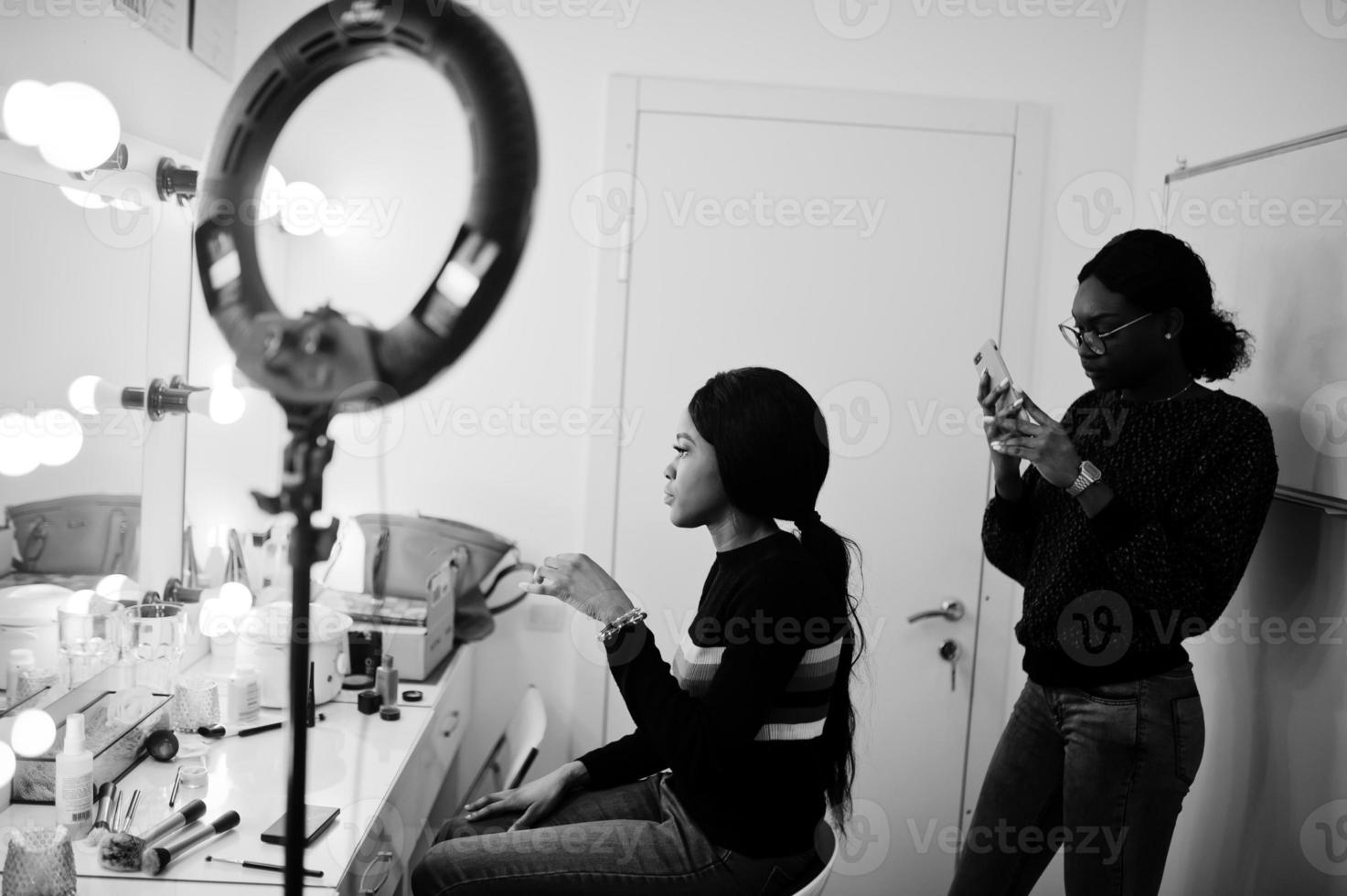 African American woman applying make-up by make-up artist at beauty saloon. photo