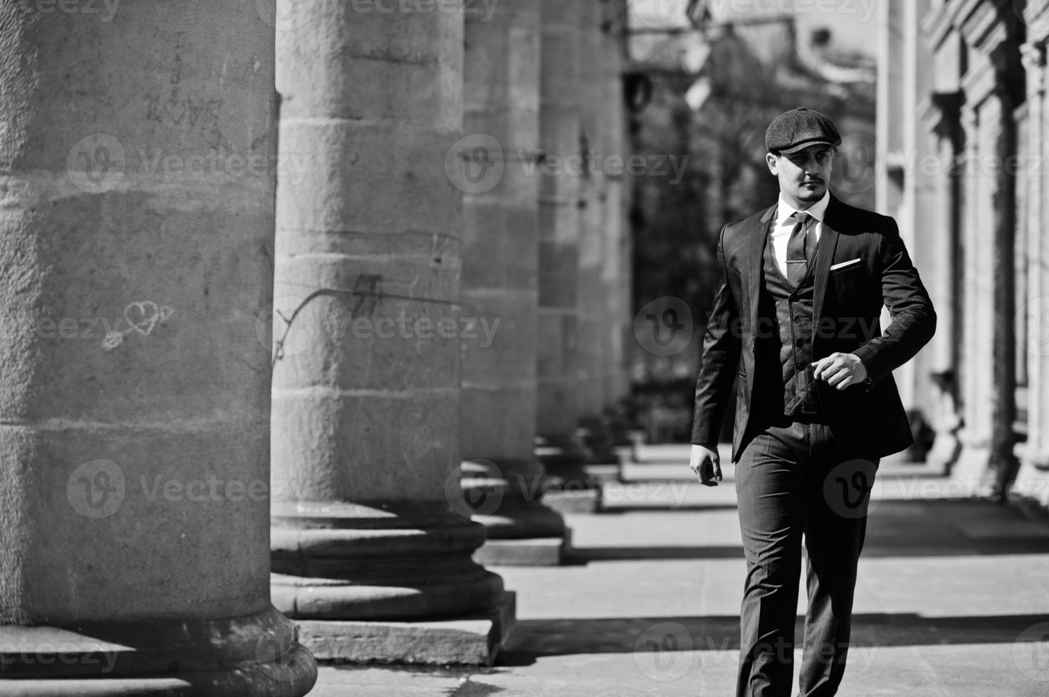 retrato de un hombre de negocios árabe inglés retro de los años 20 con traje oscuro, corbata y gorra plana cerca de columnas antiguas. foto