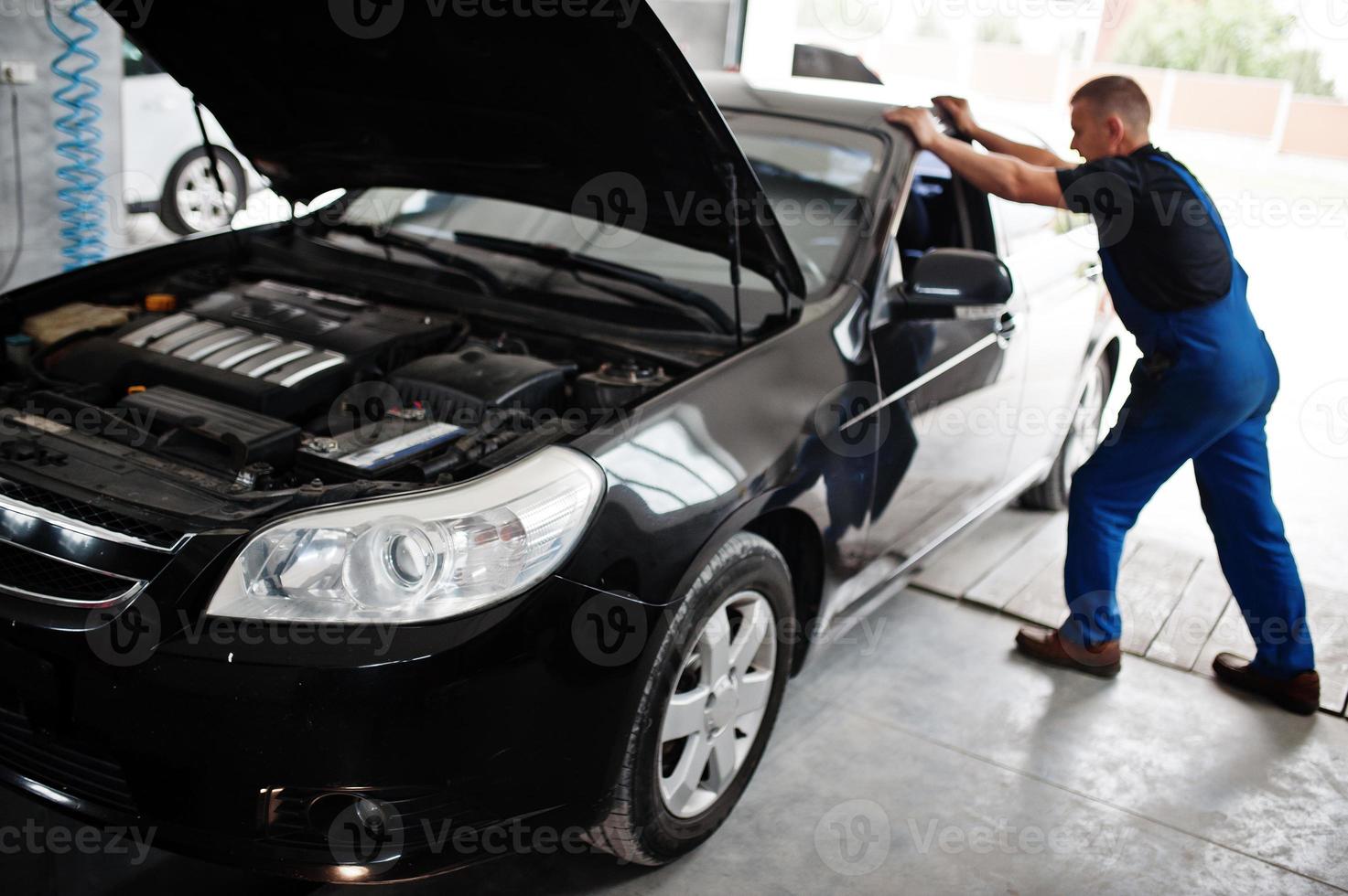 Car repair and maintenance theme. Mechanic in uniform working in auto service. photo