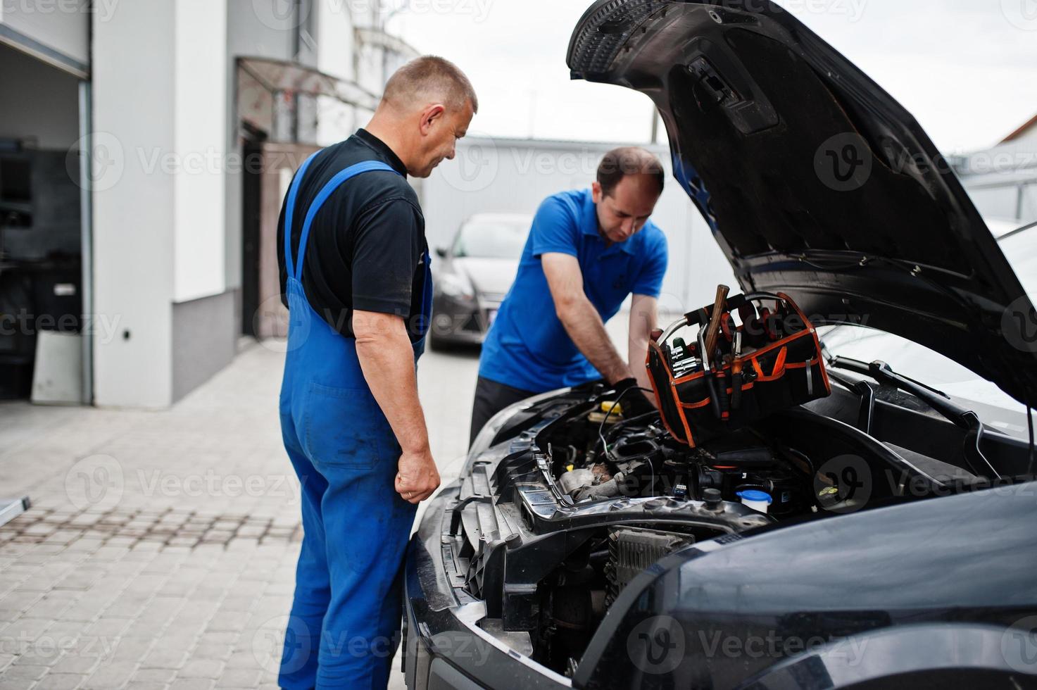 tema de reparación y mantenimiento de automóviles. dos mecánicos uniformados trabajando en autoservicio, revisando el motor. foto