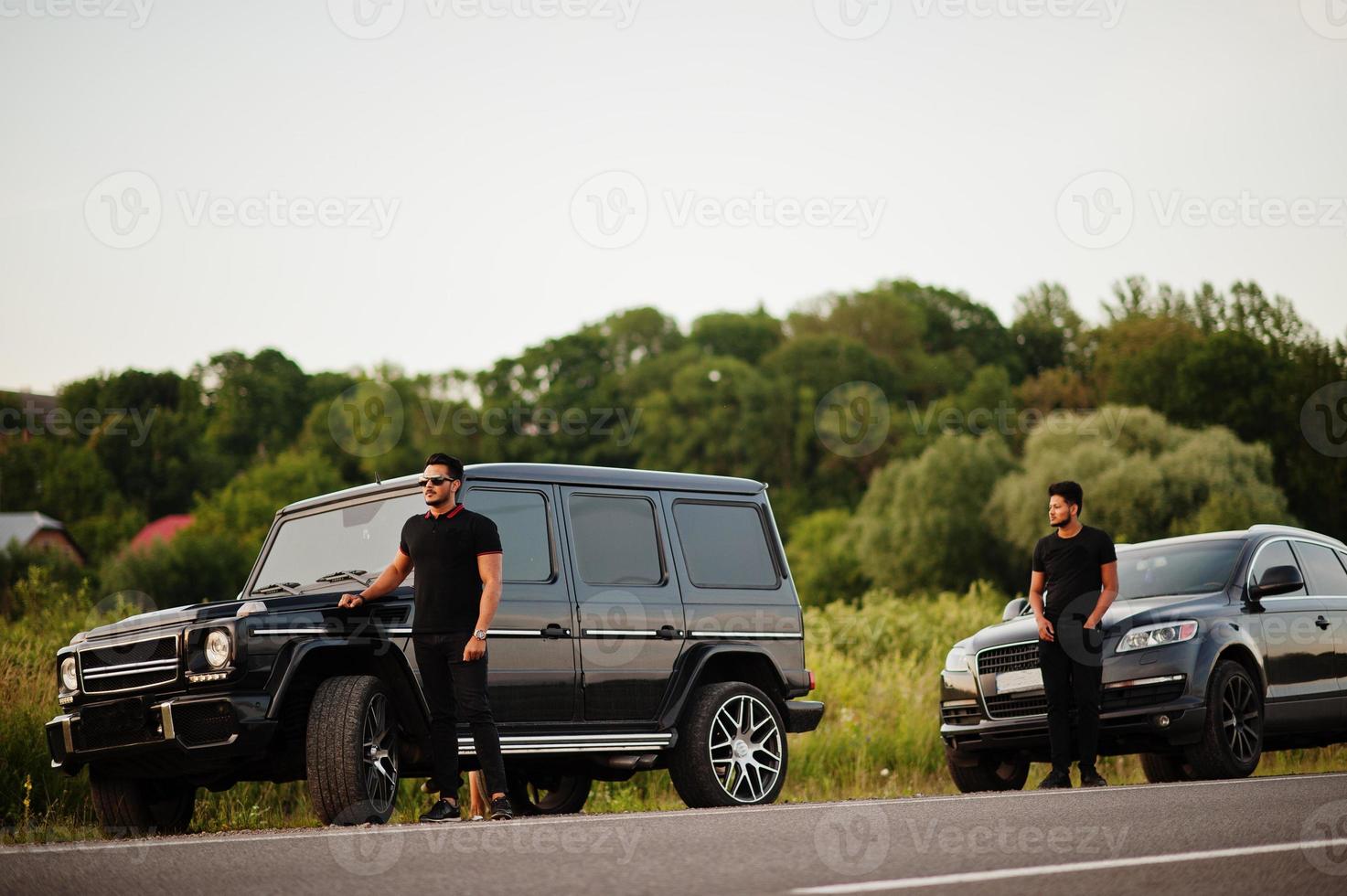 dos hermanos asiáticos se visten de negro y posan cerca de los autos todoterreno. foto