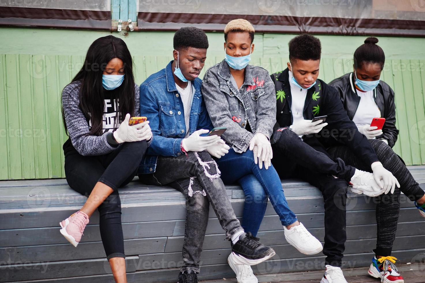 Group of african teenagers friends sitting with phones, wearing medical masks protect from infections and diseases coronavirus virus quarantine. photo