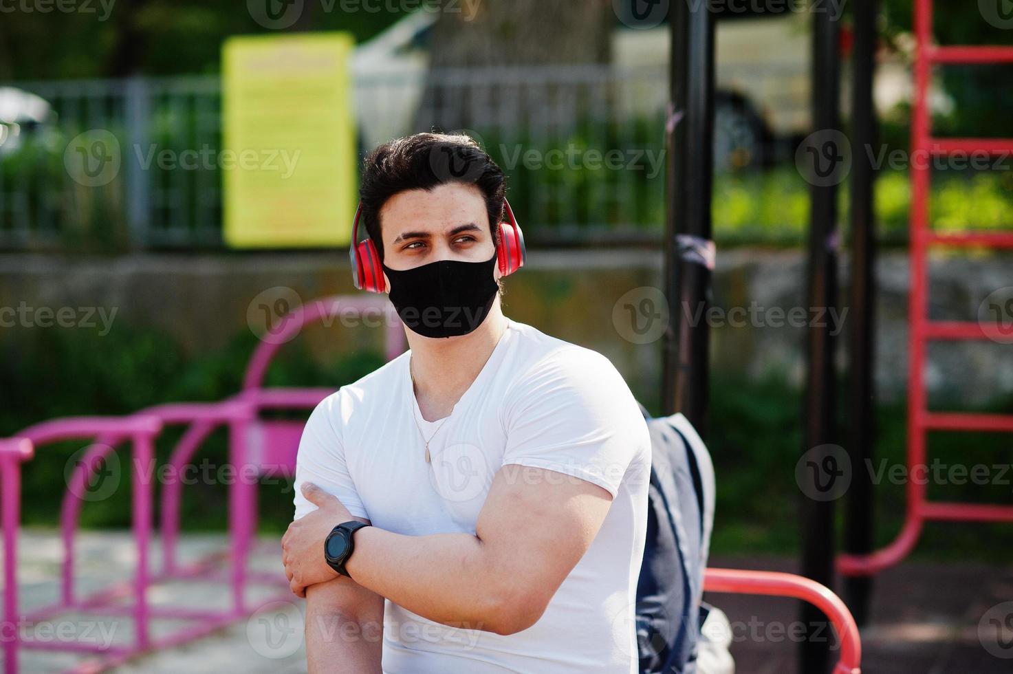 Portrait sports arabian man in black medical face mask posed outdoor with earphones during coronavirus quarantine. photo