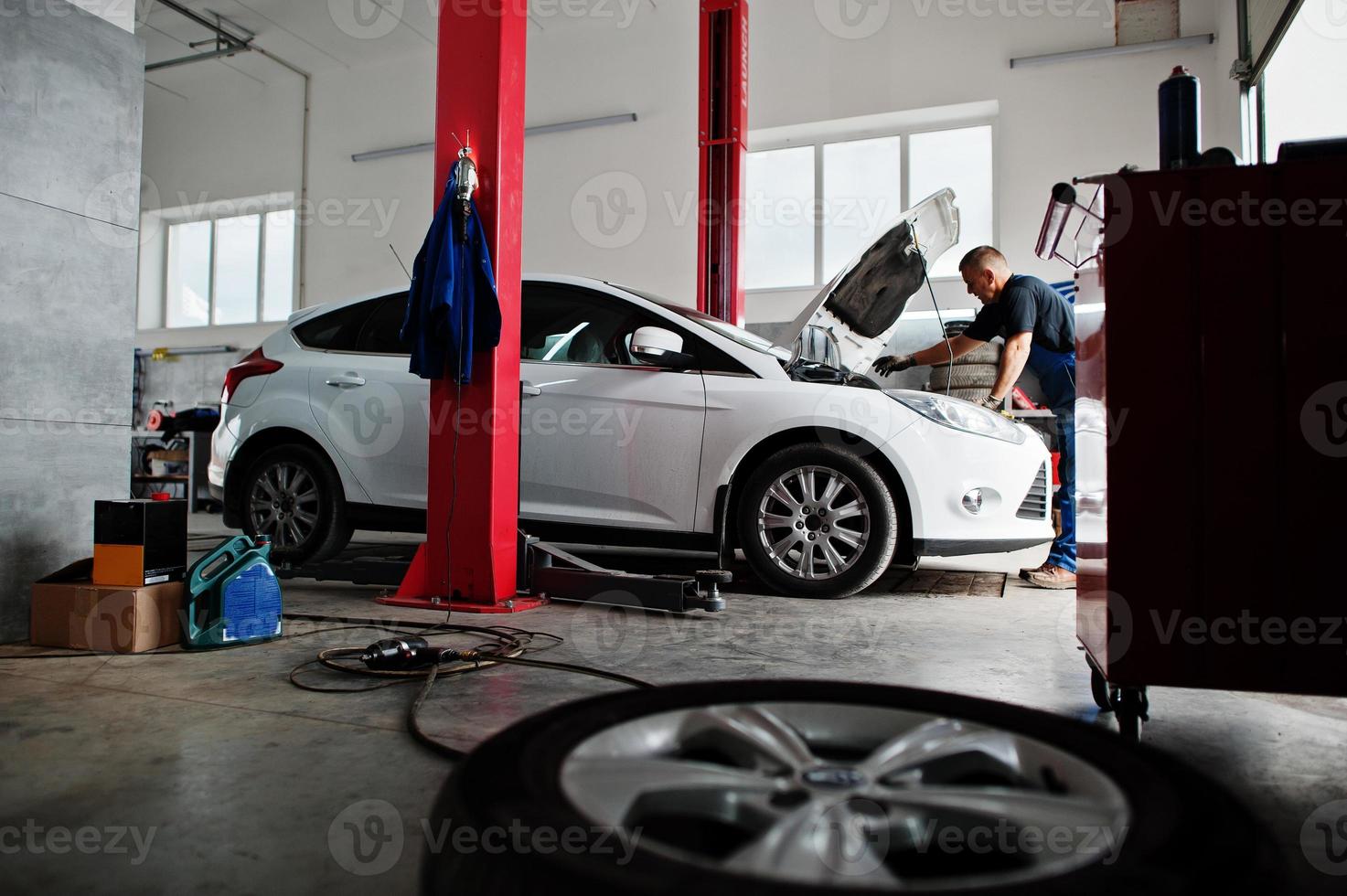 Car repair and maintenance theme. Mechanic in uniform working in auto service, checking engine. photo