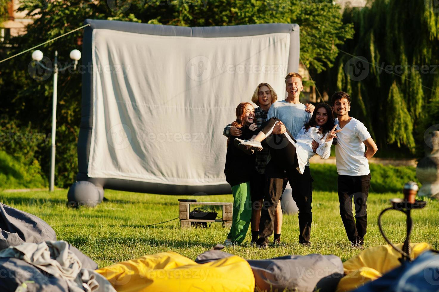 Young multi ethnic group of people watching movie at poof in open air cinema. photo