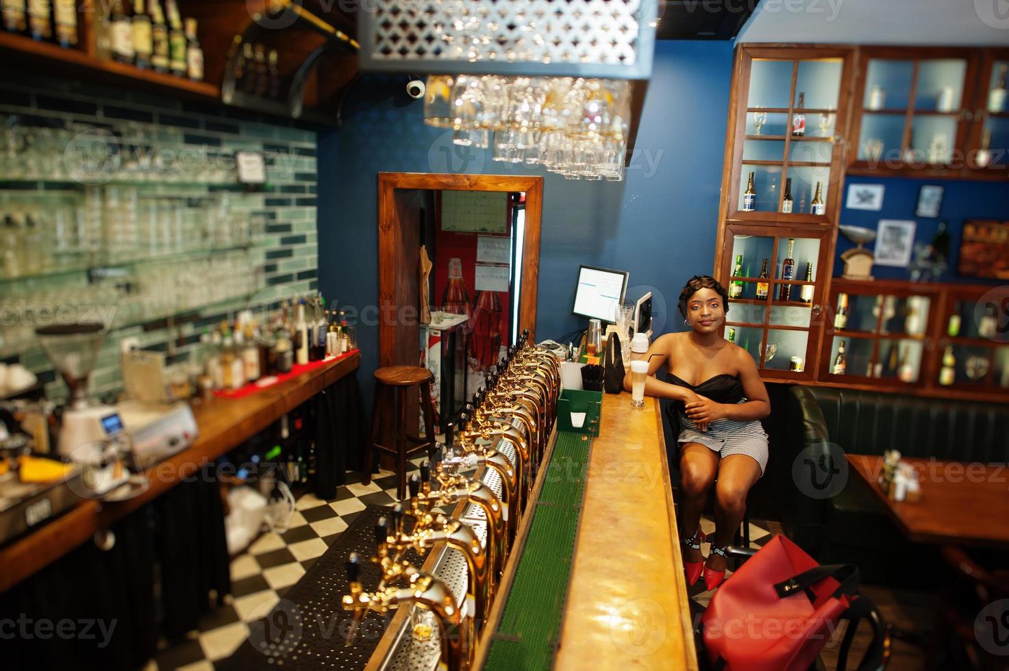 Portrait of african american woman, retro hairstyle posing at restaurant on bar counter with cup of latte. photo
