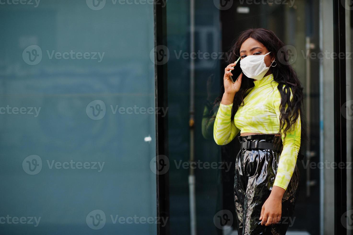 African American woman posing with facial mask to protect from infections from bacteria, viruses and epidemics and hold mobile phone. photo