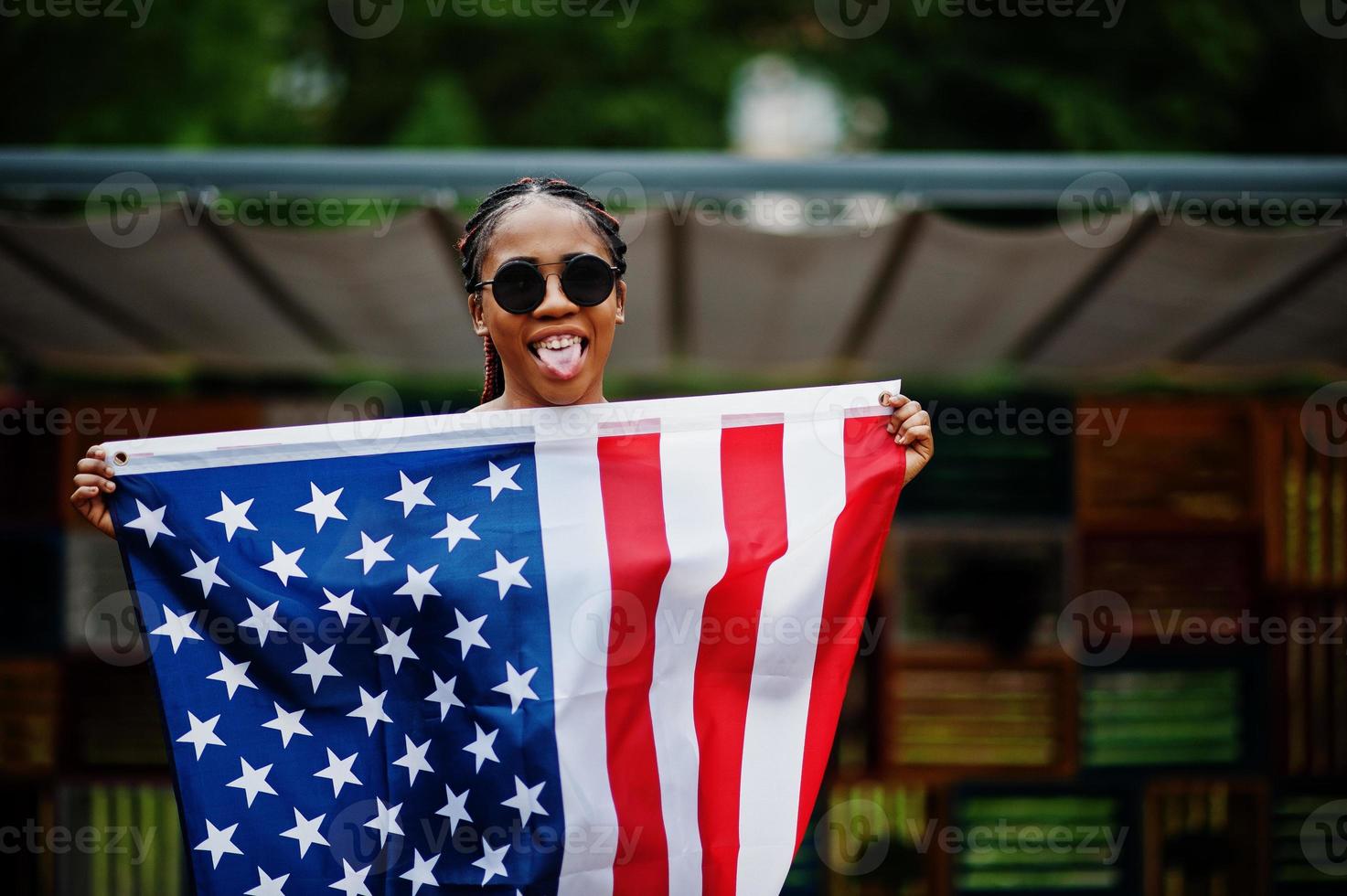 elegante mujer afroamericana con gafas de sol posadas al aire libre con la bandera de estados unidos. foto